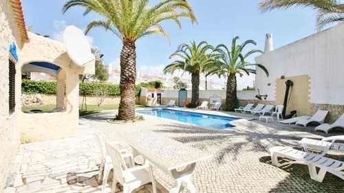 Villa pool surrounded by palm trees with outdoor dining space